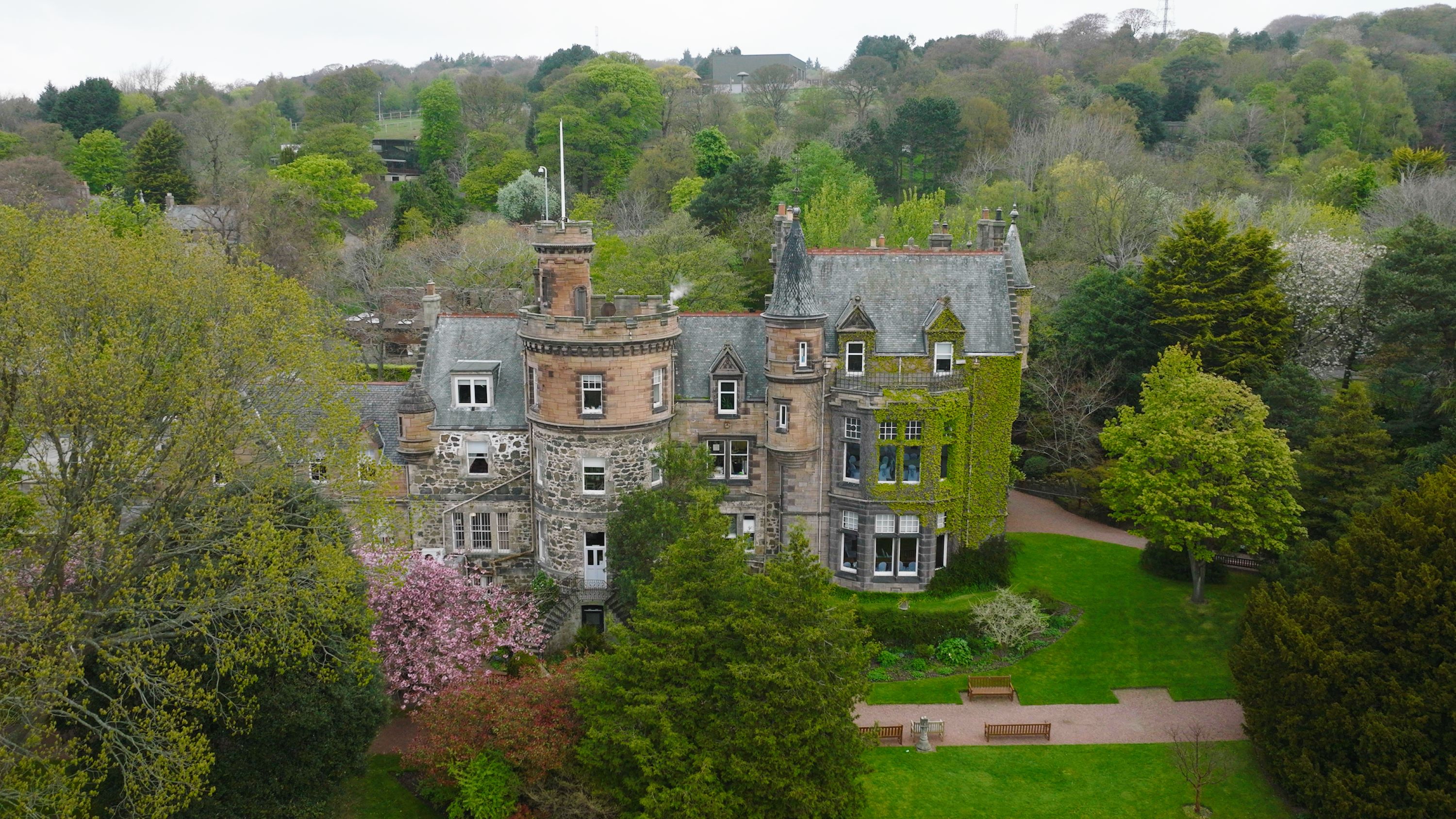 mansion house exterior drone shot with green foliage and blossom tree IMAGE: FoSho 2022